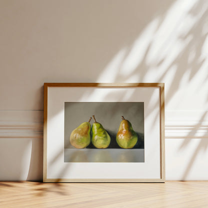 Framed fine art print of three green and yellow pears on a light gray background, leaning against a white wall.