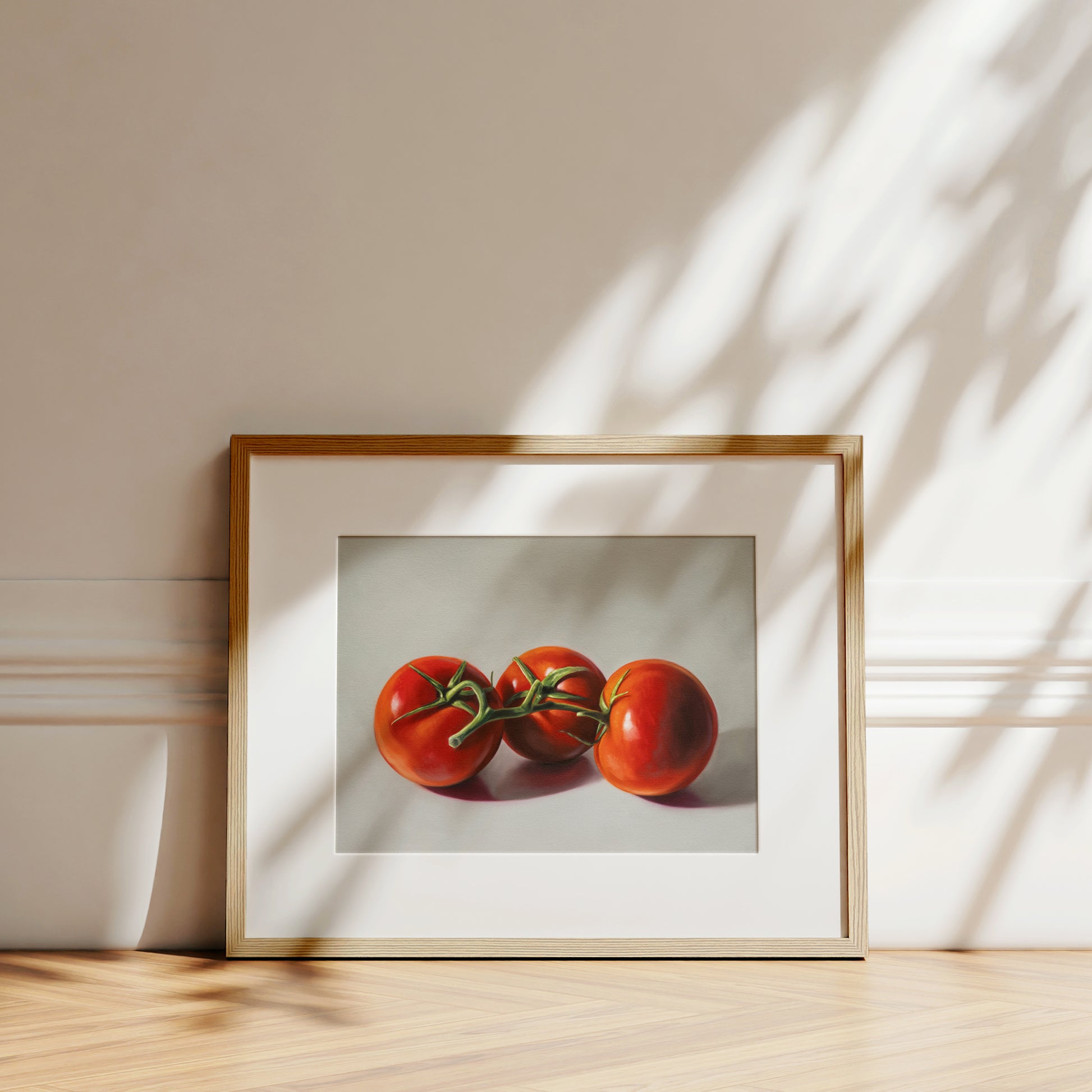 Framed fine art print of three vibrant red tomatoes on a white background, leaning against a wall.