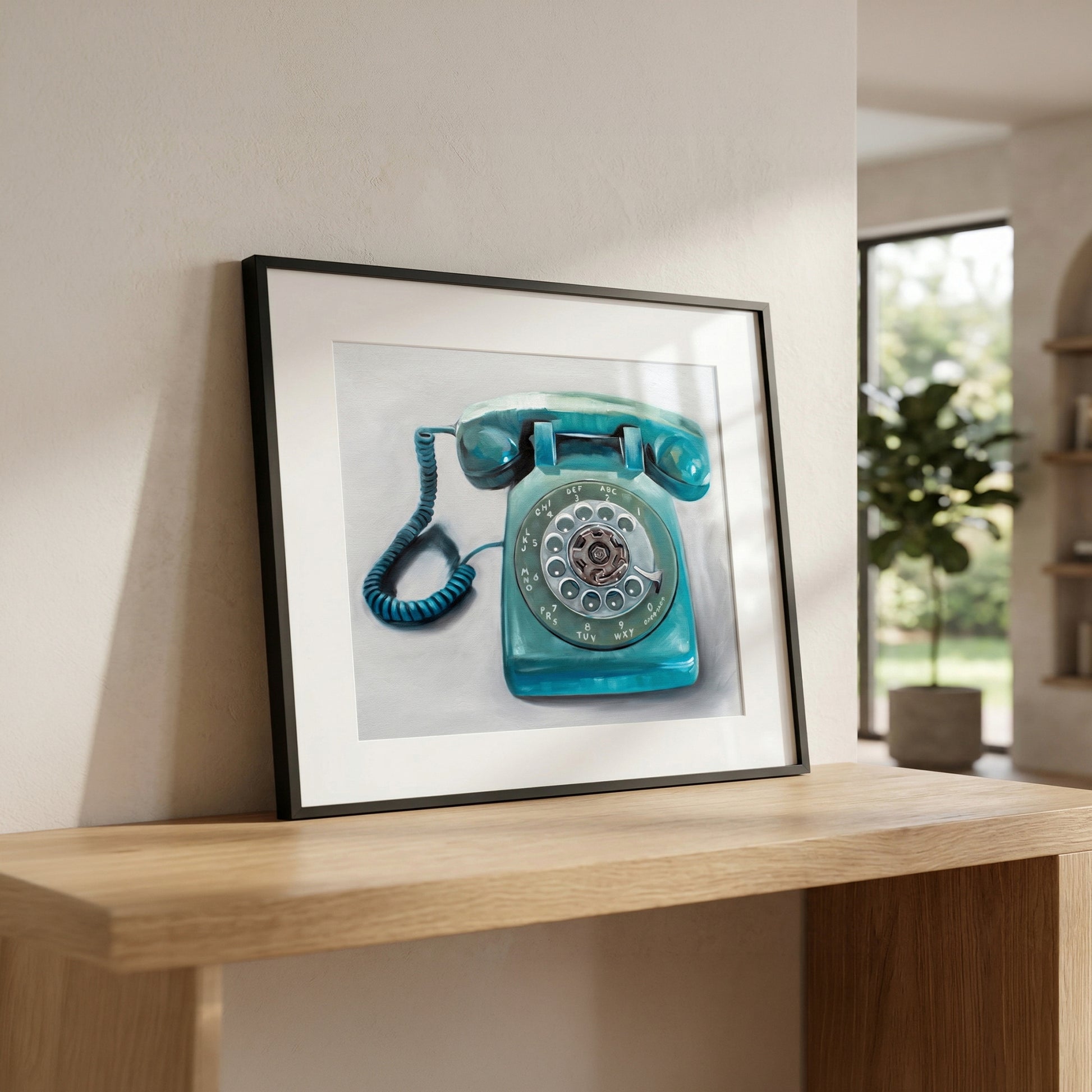 Framed fine art print of a turquoise rotary telephone on a light wood console table.