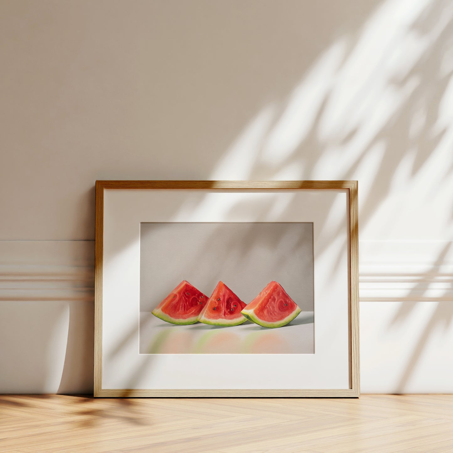 Framed fine art print of three vibrant red watermelon slices on a white background, with a light wood frame.